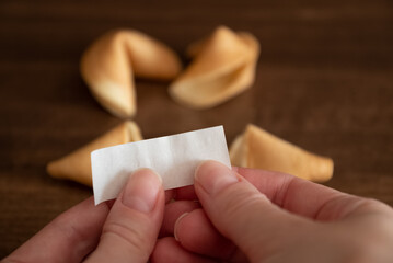 Person holds in hands blank paper slip from fortune cookie against few cookies laying on table...