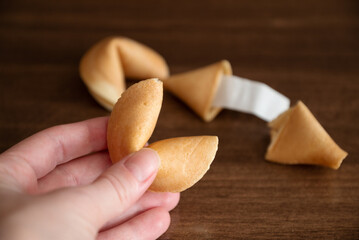 Person holding in hand fortune cookie against few cookies laying on table surface background