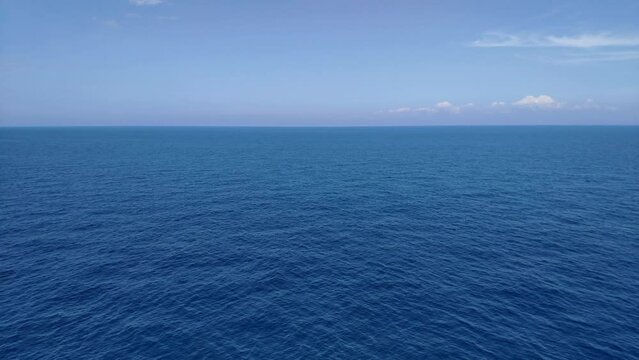 View of the horizon at open sea on a clear summer day. Water is quite still with some ondulation and there are a few coud formations in the distance.