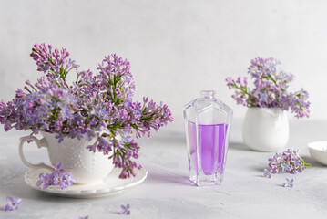 Stylish bottle of lilac perfume with spray of lilac flowers on a white background. creative floral composition. Close up. Natural perfumery and floral scent concept. Fresh spring fragrant