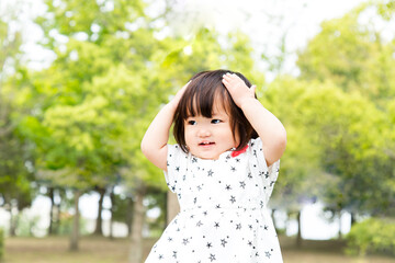 新緑の樹木を背景に笑顔で踊る幼い女の子。育児,教育,躾,愛情,幸せなイメージ
