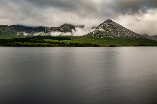 Low clouds surround the mountainous shoreline of the still and tranquil waters of Lough Inagh in Western Ireland.