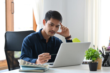 Thoughtful asian man designer working with computer laptop at creative office.