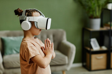 Side view portrait of tween girl practicing yoga workout in VR at home against green wall, copy...