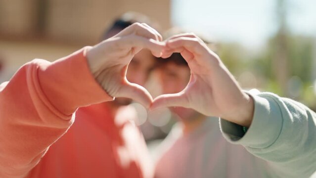 Young hispanic couple smiling confident doing heart symbol with hands at street