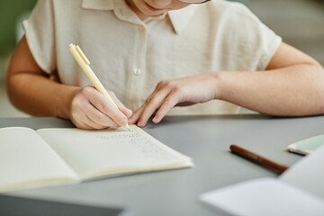 Close up of young girl writing in notebook while studying at home, copy space