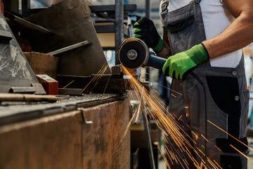 Hands holding grinder and cutting metal at workshop.