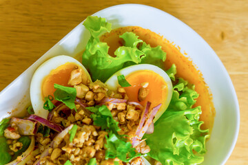 Spicy salad with boiled egg in white dish on wood table