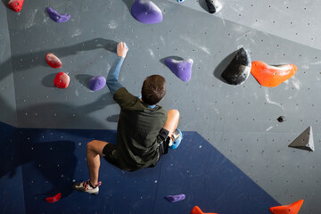 Back view of young athlete bouldering on artificial wall. Concentrated guy training in bouldering...