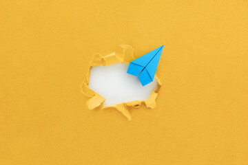 Blue paper plane breaking through paper yellow background, Business for solution, overcoming barriers, goal, target concept