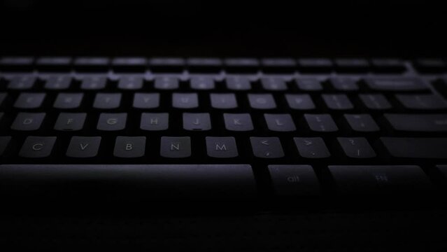Panning shot of a keyboard lit by a computer screen. 