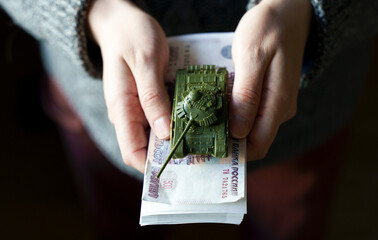 Russian rubles banknotes and toy tank in hands during the war in Ukraine. Inflation, sanctions and...