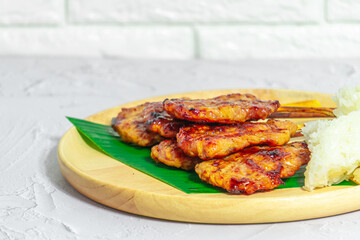 Grilled pork on bamboo skewers placed on a steel grill in a wooden tray with sticky rice in the cart, ready to serve