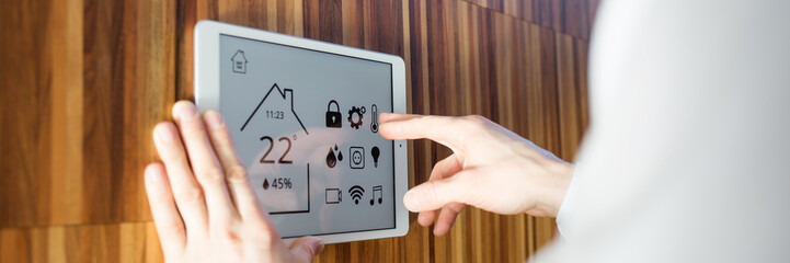 man controls smart home devices using digital tablet with launched application on background of...