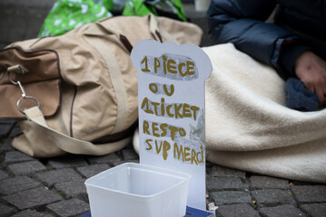 Closeup of homeless placard with text in french : un euro ou un ticket restaurant svp merci, in english : a euro or a restaurant ticket please thank you - 492513304