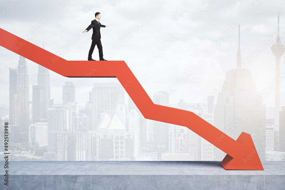 Poster businessman standing and balancing on abstract red downward chart arrow on light city background wit