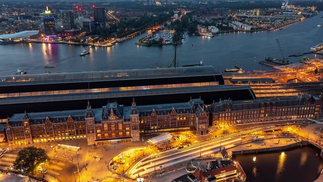 Amsterdam Netherlands Aerial v1 night hyperlapse of urban cityscape, done flyover old heritage central railway transit station with busy road traffics, incoming trains and ferries - August 2021