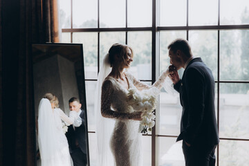 The first meeting of the groom in a black suit and the bride in a white wedding dress with a bouquet in the interior of a photo studio, hotel, on black background