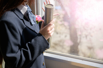 卒業式の賞状と窓辺で桜を見つめる女子高生