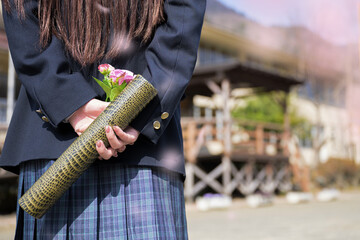 学校の前で卒業証書を持つ学生　アップ　桜の前ボケ