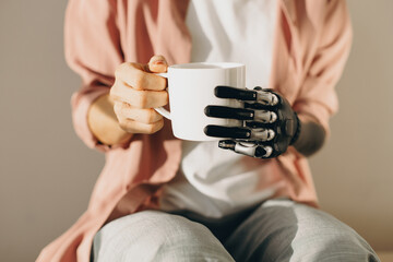 Artificial bionic female hand with mechanical metal fingers holding cup of hot drink in white cup....