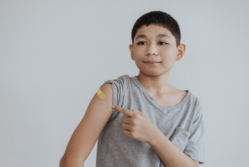 Asian boy showing shoulders after getting a vaccine. Happy little boy showing arm with band-aids on...
