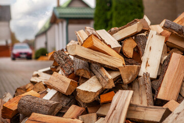 A pile of split firewood for heating the house, unloaded in the yard, against the backdrop of the house, natural heating sources.