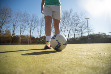 Close-up of female football player with ball on field. Low angle view of teenage girls legs in sport shoes standing on stadium getting ready for playing football. Sport and healthy lifestyle concept