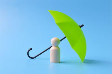 Green toy umbrella and wooden doll figure isolated on a blue background