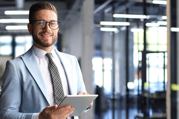 Modern business man in formalwear using digital tablet while standing near window in the office