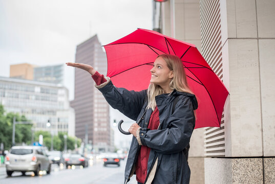 Smiling young woman with red umbrella enjoying rain