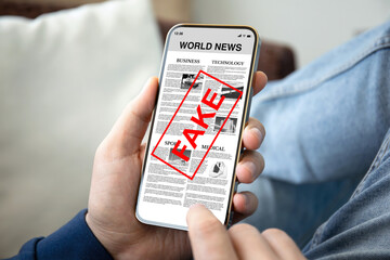 male hands hold phone with world news and word fake