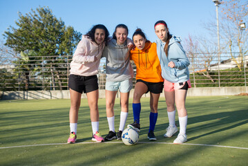 Portrait of female football team posing on field.Four pretty and sporty girls in sportswear standing together hugging showing their unity and looking at camera.Team sport and healthy lifestyle concept