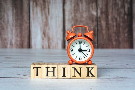 Think text on wooden blocks and alarm clock set at 3 o'clock on table.