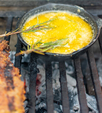mantequilla derretida con romero  en sarten de hierro  sobre la parrilla. 

mantequilla derretida condimentada en el asador.