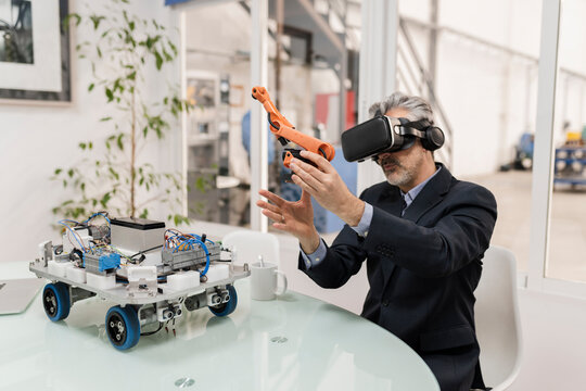 Businessman wearing virtual reality holding robotic arm model sitting at desk