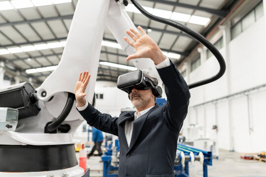 Businessman wearing virtual reality simulator standing with arms raised in factory