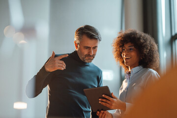 Happy working woman discussing with colleague over tablet PC at work place