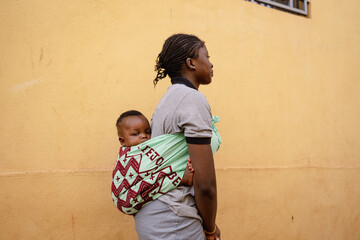 Underage African girl with a baby on her back walking down the street; symbol for forced marriage...