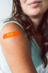 woman showing covid-19 vaccination band-aid on her arm, protection from the pandemic and coronavirus health risks