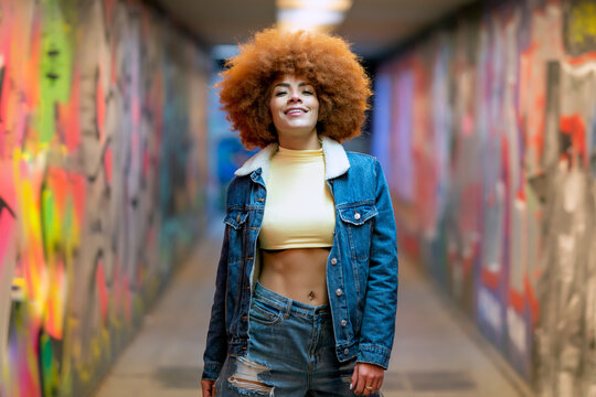 Smiling woman with Afro hairstyle standing by graffiti wall