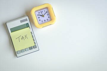 The word Tax on yellow adhesive paper, stick on calculator next to a yellow clock. Top view. Tax filing concept.