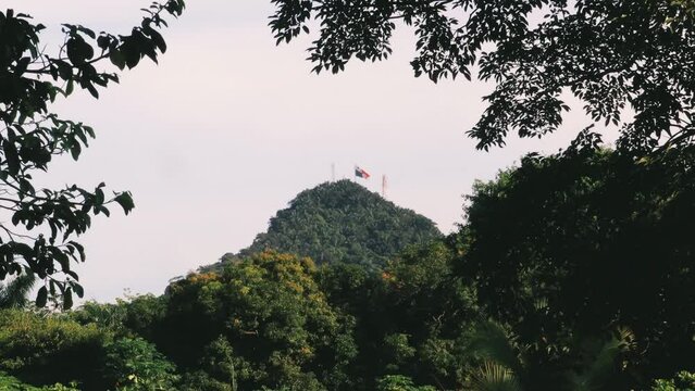 Huge flag of Panama on top of famous Ancon Hill in Panama's Capital City in a beautiful sunny summer morning, viewed from a dense rich green vegetation portraying the inmense biodiversity it has
