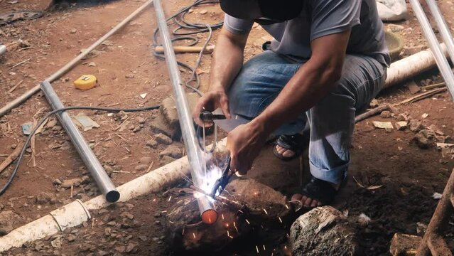 Professional welder employing industrial welding machine to put together two pieces of metal creating a metalic structure as part of his daily work at a local small business