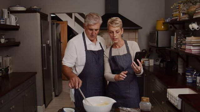 Elderly couple baking in kitchen using cellular device 