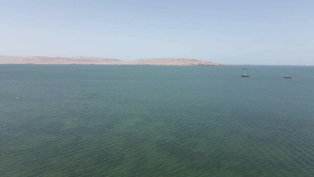 Fishing boats work in shallow green bay off desert coast in Peru