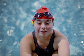 Young woman with Down syndrome swimming in swimming pool and looking at camera