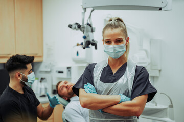 Fototapeta na wymiar Caucasian female dentist wearing surgical mask standing with arms crossed in doctors room 