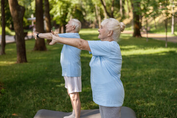 Sportive senior lady with partner train together standing on lush lawn