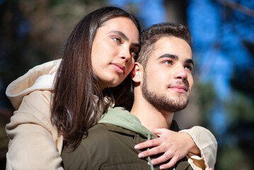 Portrait of young affectionate couple hugging in forest. Woman with dark hair hugging bearded man on shoulders. Love, affection, relationship concept